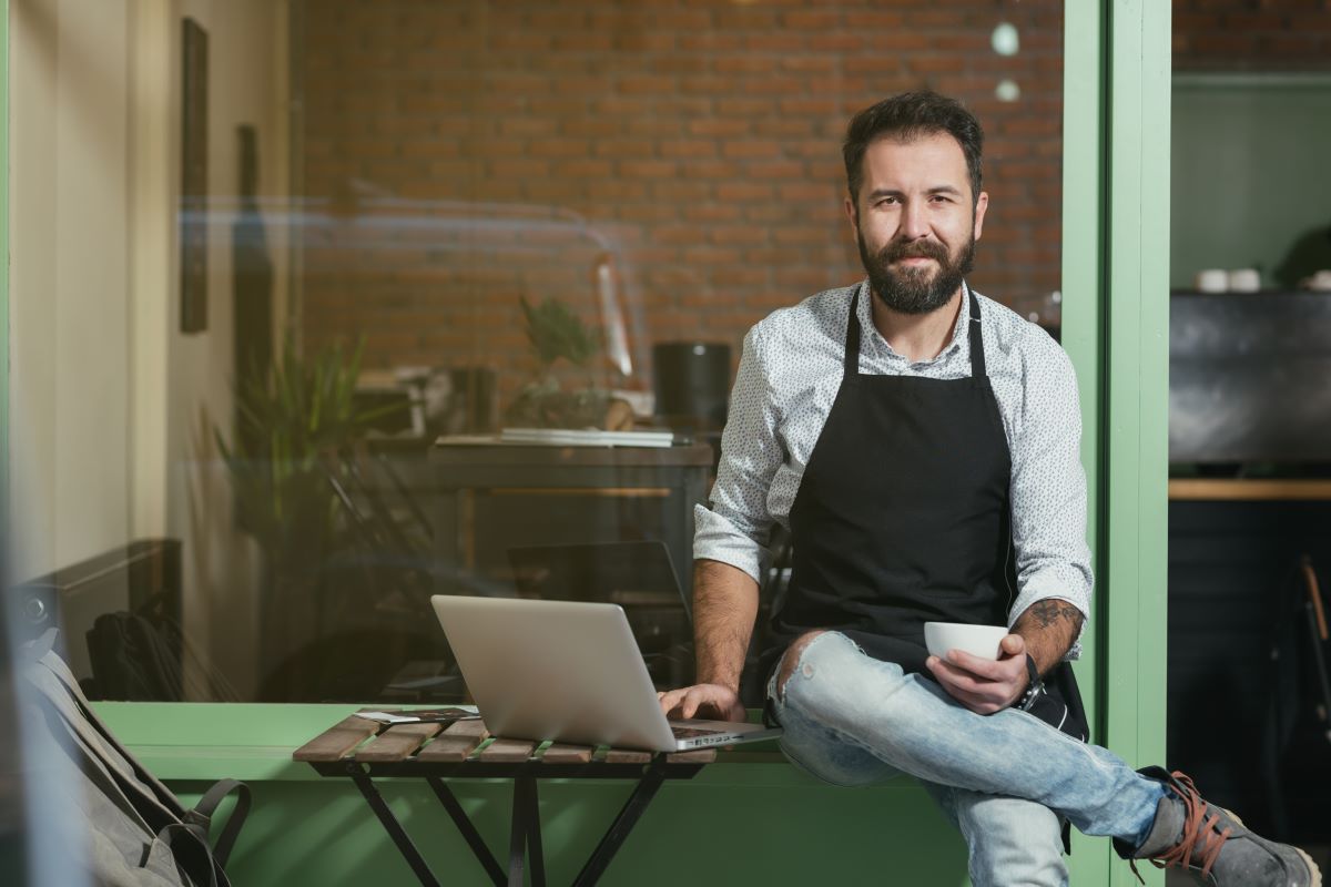 man using laptop while holding a cup outside a cafe