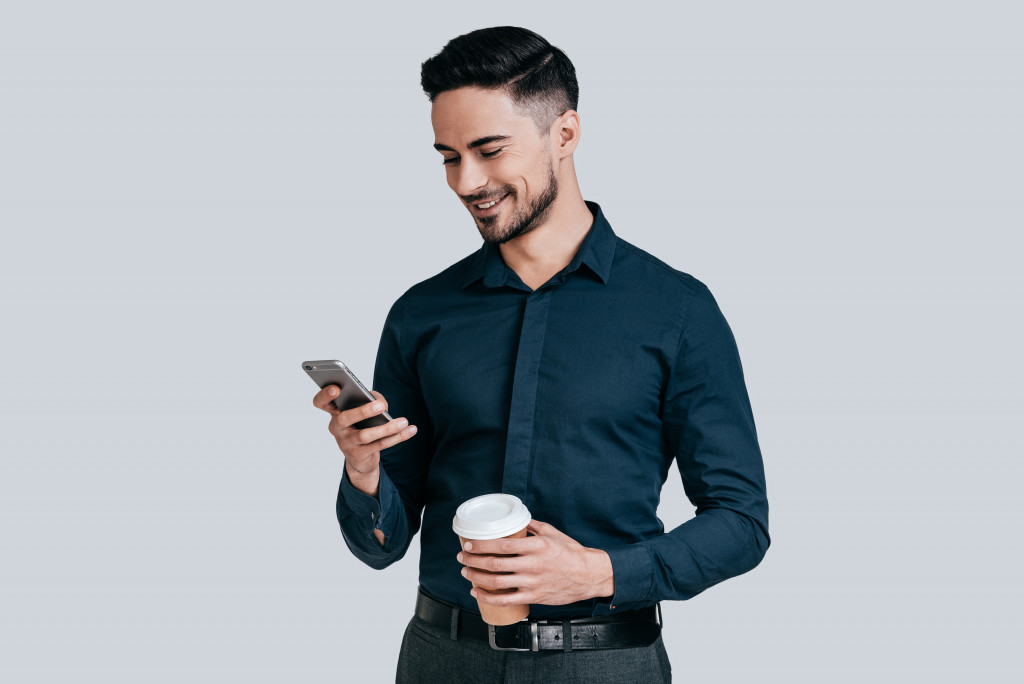 man holding coffee and using mobile phone