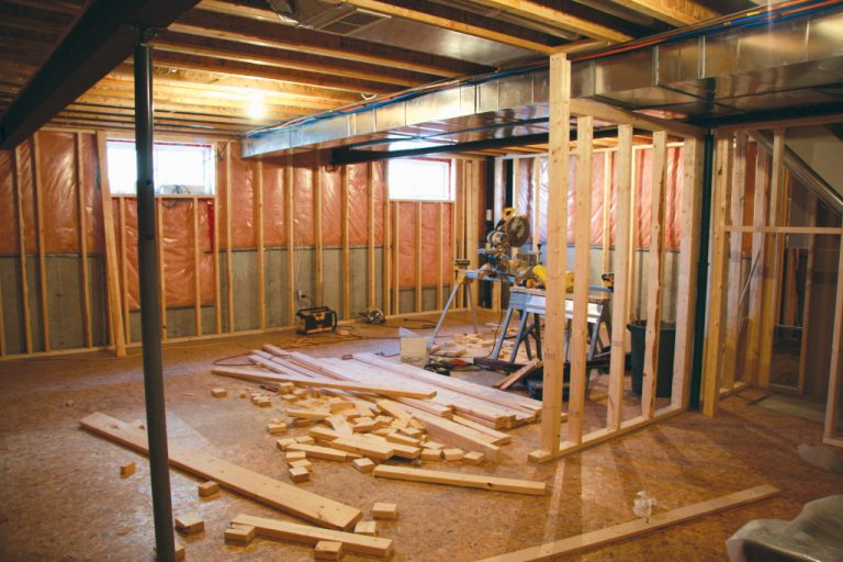 A well-lit basement under renovation with exposed wood, pipes, and ventilation