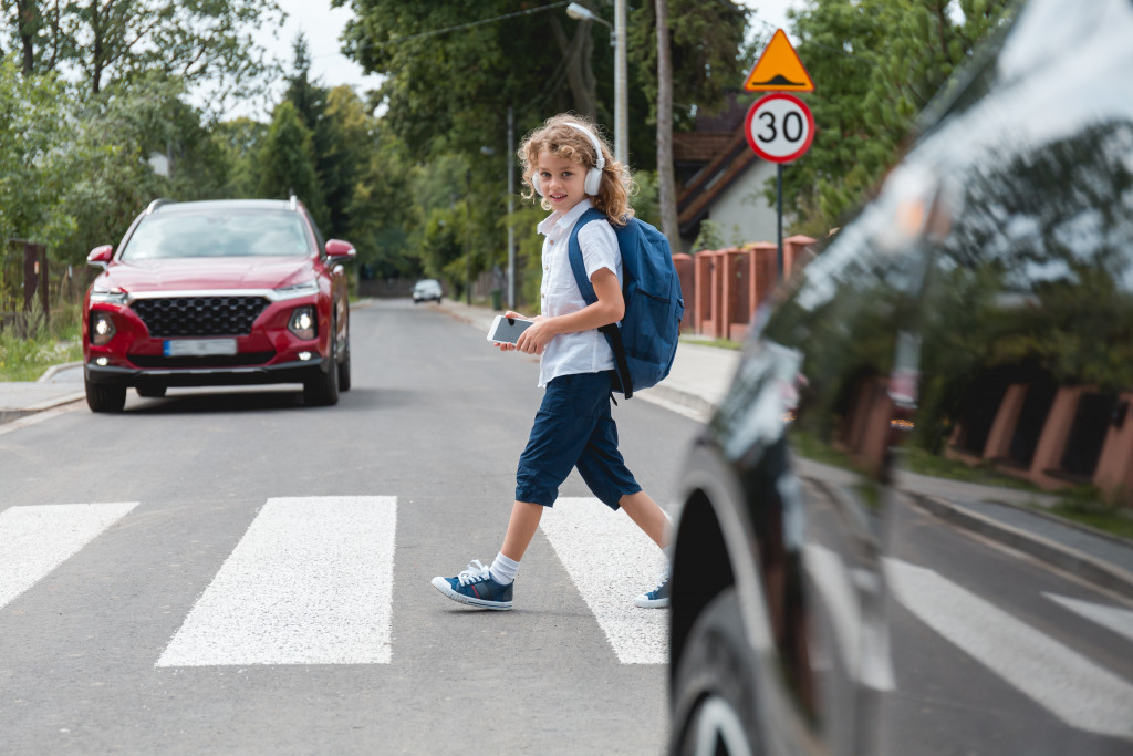 a young boy at a pedestrian crossing wearing headphones and backpack