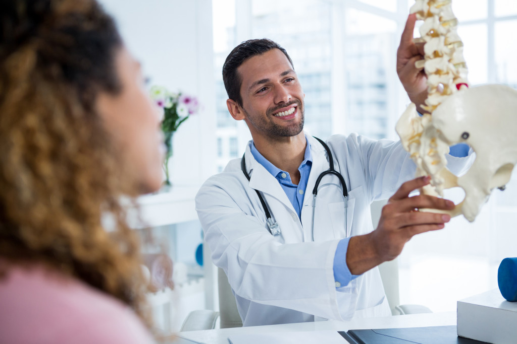 A doctor holding a spine model and showing it to a patient