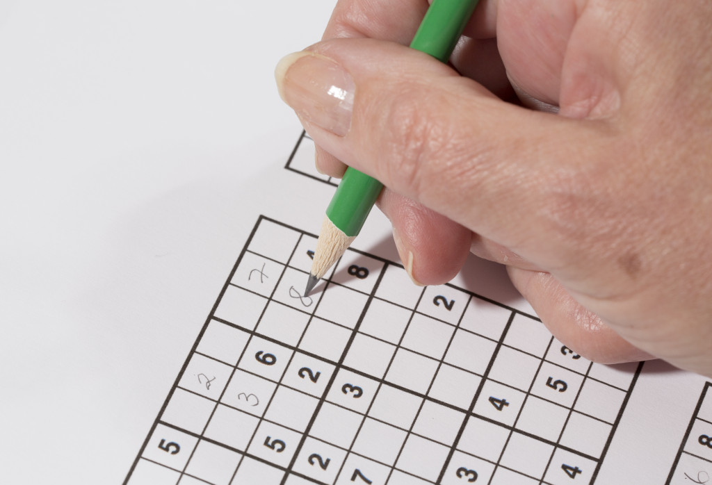 An elderly person using a pencil to answer a sudoku puzzle