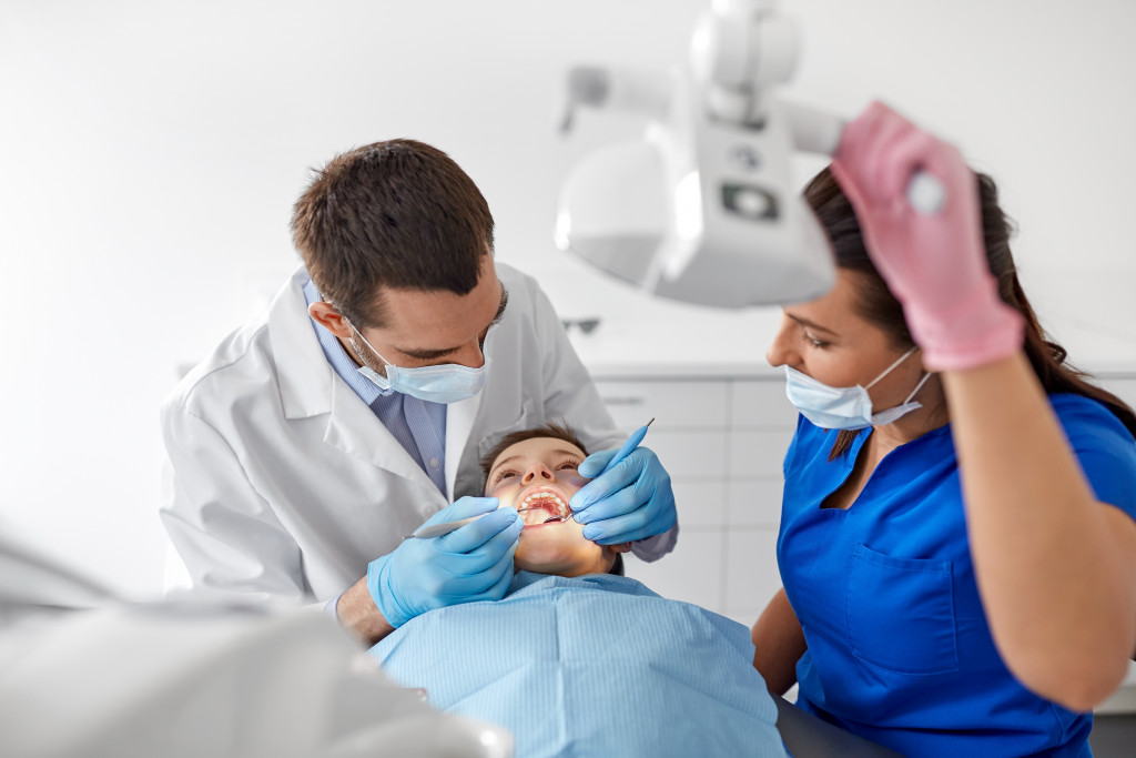 Dentist checking the teeth of a patient with an assistant looking on.