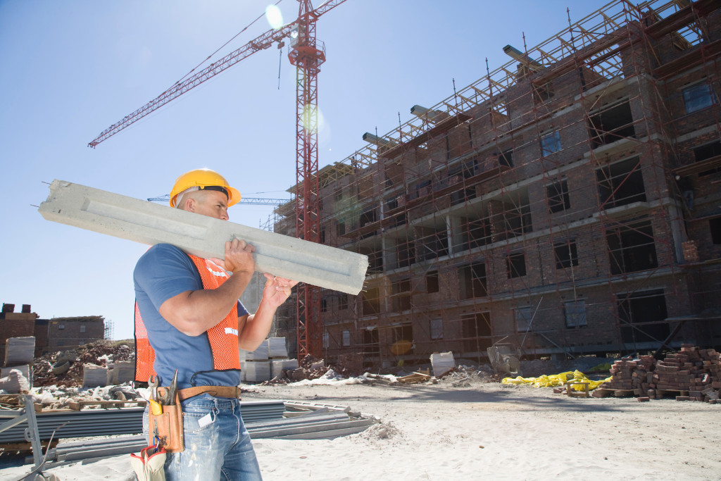 A laborer, construction worker carrying a concrete beam in a construction site