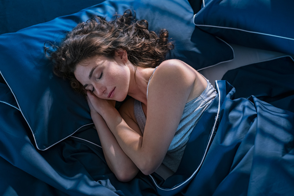 Young woman sleeping soundly at night on a blue bed with blue covers.