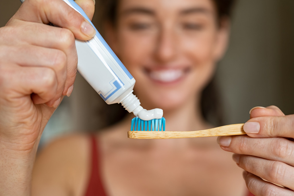 Young woman putting toothpaste on a wooden toothbrush at home.