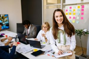 smiling woman in professional attire with colleagues working in the background